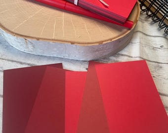 May include: Four red cardstock sheets in different shades of red, from dark red to bright red. The sheets are arranged in a fan shape, with the darkest red sheet at the bottom and the brightest red sheet at the top.