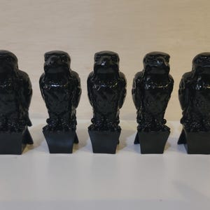 May include: Five identical black figurines, each depicting a bird of prey perched on a square base. The birds have detailed feathers, sharp beaks, and forward-facing eyes, all rendered in a glossy, solid black finish standing in a row.