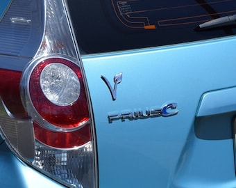 May include: A light blue Toyota Prius C with a chrome "Prius C" emblem and a green leaf logo on the back.