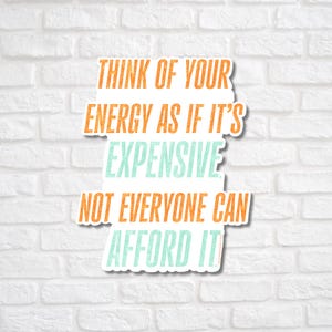 May include: A white sticker with the text "THINK OF YOUR ENERGY AS IF IT'S EXPENSIVE NOT EVERYONE CAN AFFORD IT" in orange and teal lettering. The sticker is against a white brick wall.