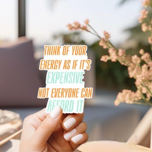 May include: A white sticker with the text "Think of your energy as if it's expensive, not everyone can afford it" in orange and teal lettering. The sticker is held by a hand with white nail polish.