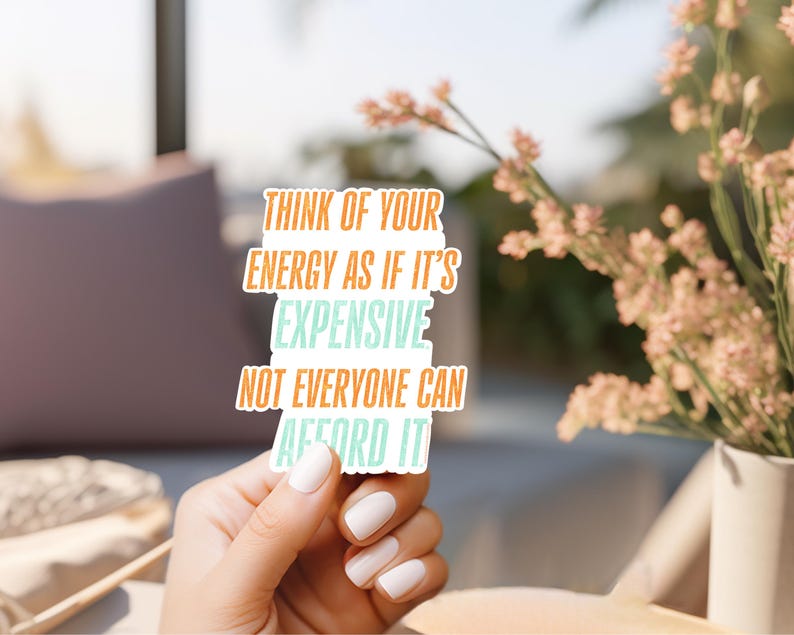 May include: A white sticker with the text "Think of your energy as if it's expensive, not everyone can afford it" in orange and teal lettering. The sticker is held by a hand with white nail polish.