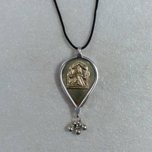 May include: A silver pendant necklace with a teardrop-shaped pendant featuring a gold-toned image of a deity. The pendant is attached to a black cord.