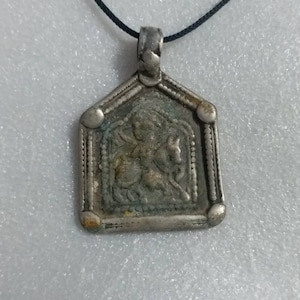 May include: A silver pendant necklace with a detailed image of a person riding a horse. The pendant is framed with a decorative border and has a black cord.