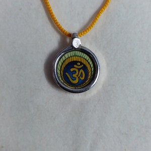 Pittura artistica in miniatura indiana dipinta a mano fatta a mano, pendente Om in argento sterling 92,5 con cornice in vetro, divinità con piuma di pavone e cordino colorato.