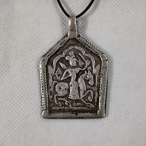 May include: A silver pendant necklace with a black cord. The pendant is shaped like a house and features an intricate design of a person riding a horse.