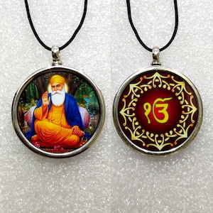 May include: A silver pendant necklace with two sides. One side features a colorful image of a man with a beard and turban. The other side features a red background with a gold symbol.