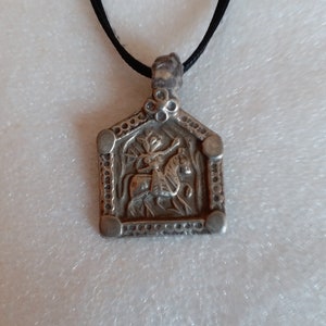 May include: A silver pendant necklace with a black cord. The pendant features a detailed design of a person riding a horse.