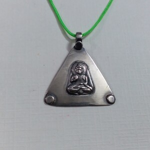 May include: A silver triangle pendant necklace with a small, embossed image of a person sitting in a meditative pose. The necklace is on a green cord.