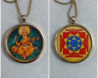 May include: A gold chain necklace with a round pendant featuring a colorful image of a goddess playing a stringed instrument on one side and a red and gold mandala on the other side.