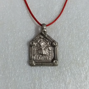 May include: A silver pendant necklace with a red cord. The pendant features a detailed design of a figure on horseback.