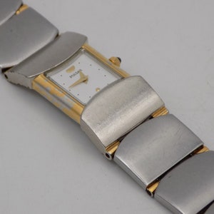 Puede incluir: Un reloj de pulsera Pulsar de dos tonos, plateado y dorado, con una esfera blanca y una pulsera de metal plateado.
