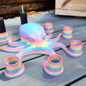 May include: A colorful octopus-shaped candle holder with rainbow-colored tentacles and candle cups. The word "KRAKEN" is printed on the base. Two black candle holders are also included. The octopus is painted in pastel colors.