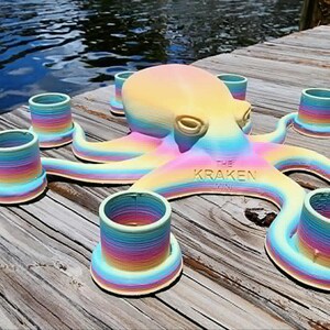 May include: A colorful octopus-shaped candle holder with eight candle cups. The octopus is painted in a rainbow gradient of colors, with the text "THE KRAKEN" on its body. The holder is placed on a wooden dock.