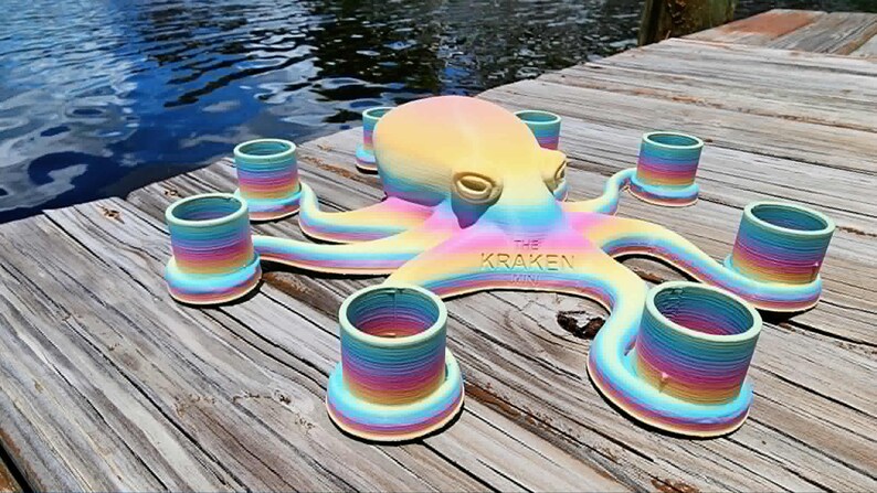 May include: A colorful octopus-shaped candle holder with eight candle cups. The octopus is painted in a rainbow gradient of colors, with the text "THE KRAKEN" on its body. The holder is placed on a wooden dock.
