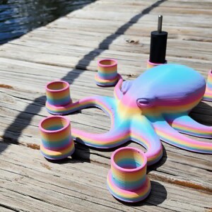 May include: A colorful octopus-shaped candle holder with rainbow-striped tentacles and matching candle cups. The octopus is painted in pastel shades of blue, purple, and yellow. The candle holders are on a wooden surface.