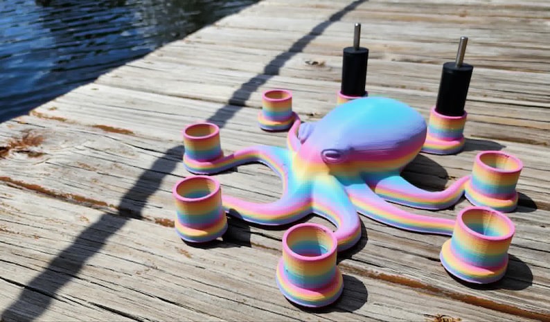 May include: A colorful octopus-shaped candle holder with rainbow-striped tentacles and matching candle cups. The octopus is painted in pastel shades of blue, purple, and yellow. The candle holders are on a wooden surface.