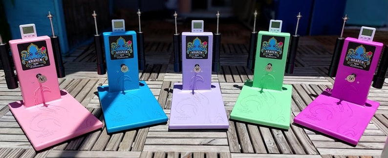 Op de afbeelding: Vijf kleurrijke elektronische apparaten met een digitaal display en een zwarte antenne. Elk apparaat heeft een basis in een andere kleur: roze, blauw, paars, groen en magenta. De apparaten hebben een afbeelding van een octopus met de tekst "Kraken" aan de voorkant.
