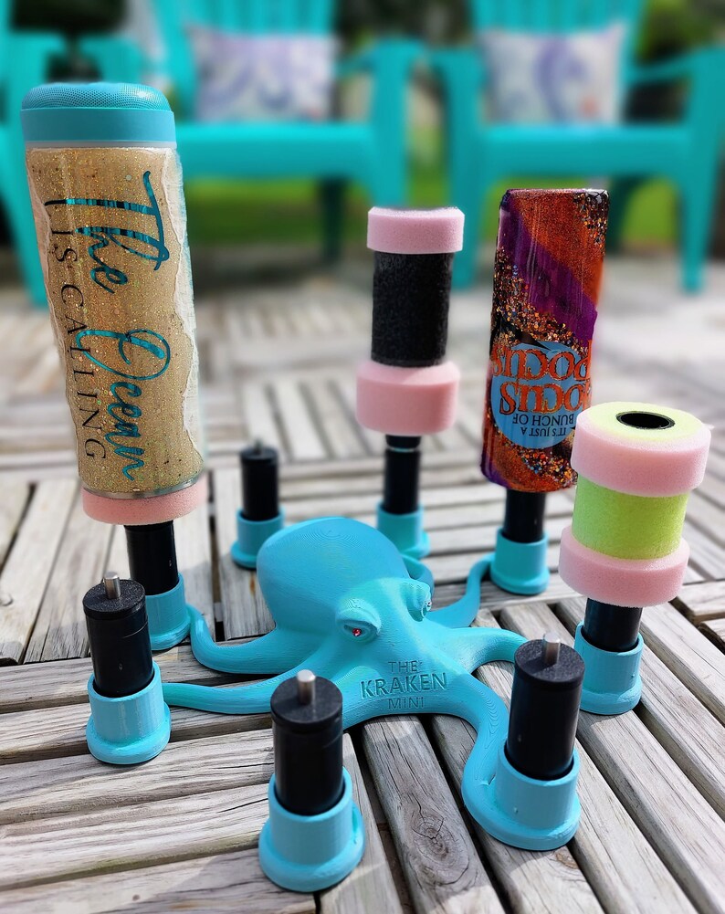 May include: A collection of decorative bottle stoppers with various designs, including glitter-filled cylinders and a teal octopus figurine. The stoppers have pink, black, and green accents. The text "The Ocean is Calling" is visible on one stopper.
