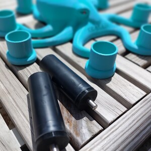 May include: A turquoise octopus-shaped sculpture with matching teal cup holders and two black cylindrical objects with silver rods. The items are arranged on a weathered wooden surface, creating a playful, aquatic-themed display.