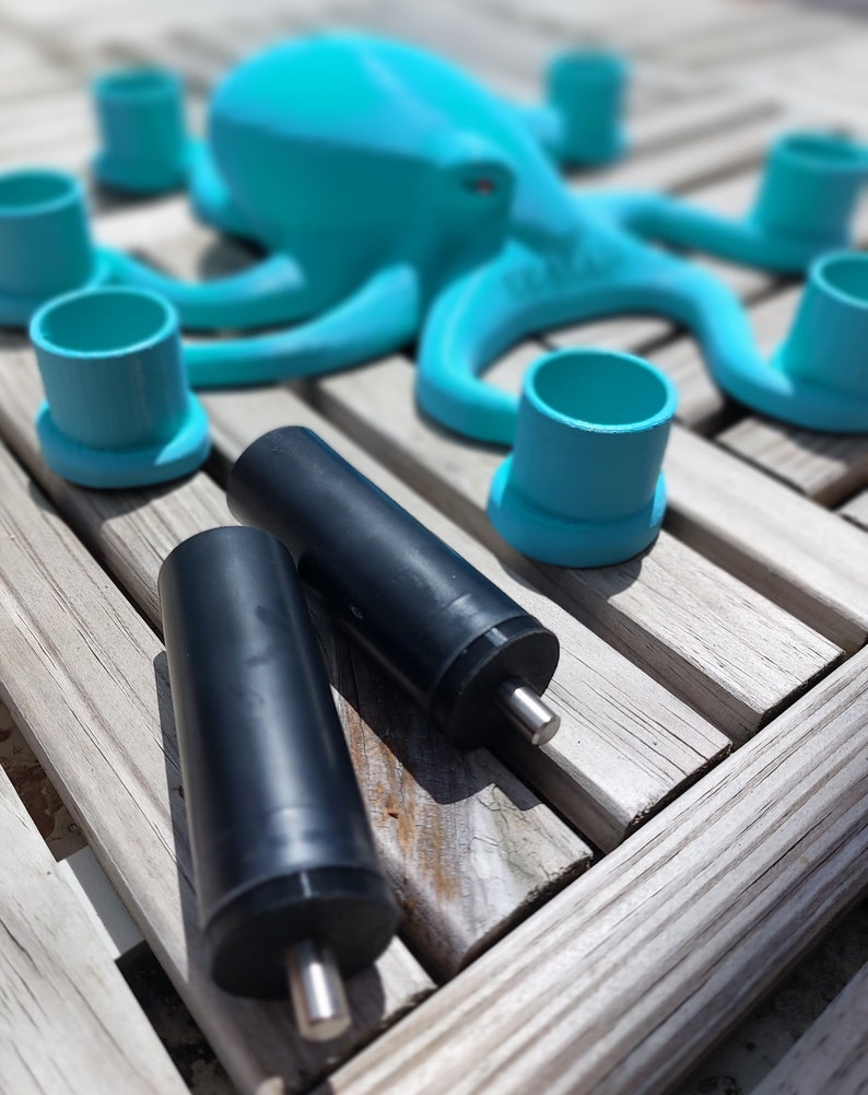 May include: A turquoise octopus-shaped sculpture with matching teal cup holders and two black cylindrical objects with silver rods. The items are arranged on a weathered wooden surface, creating a playful, aquatic-themed display.