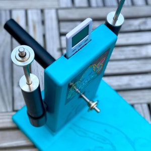Op de afbeelding: Een turquoise blauw plastic apparaat met een witte digitale timer, twee zwarte en zilveren staven en een zilveren draaiende staaf. Het apparaat heeft een afbeelding van een cartoonfiguur aan de voorkant.