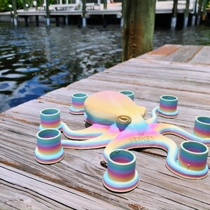 May include: A colorful octopus-shaped candle holder with rainbow-colored tentacles and candle cups. The text "THE KRAKEN" is visible on the octopus. The candle holder is sitting on a wooden dock near water.