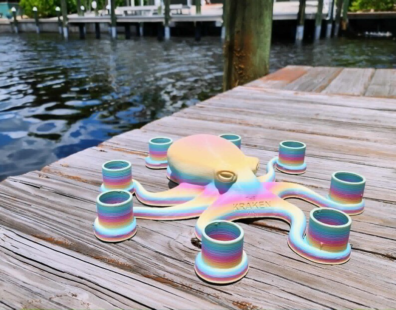 May include: A colorful octopus-shaped candle holder with rainbow-colored tentacles and candle cups. The text "THE KRAKEN" is visible on the octopus. The candle holder is sitting on a wooden dock near water.