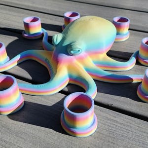 May include: A colorful octopus sculpture with eight matching cup-shaped candle holders. The octopus and candle holders are painted in a rainbow gradient of pastel colors. The sculpture is on a wooden surface.