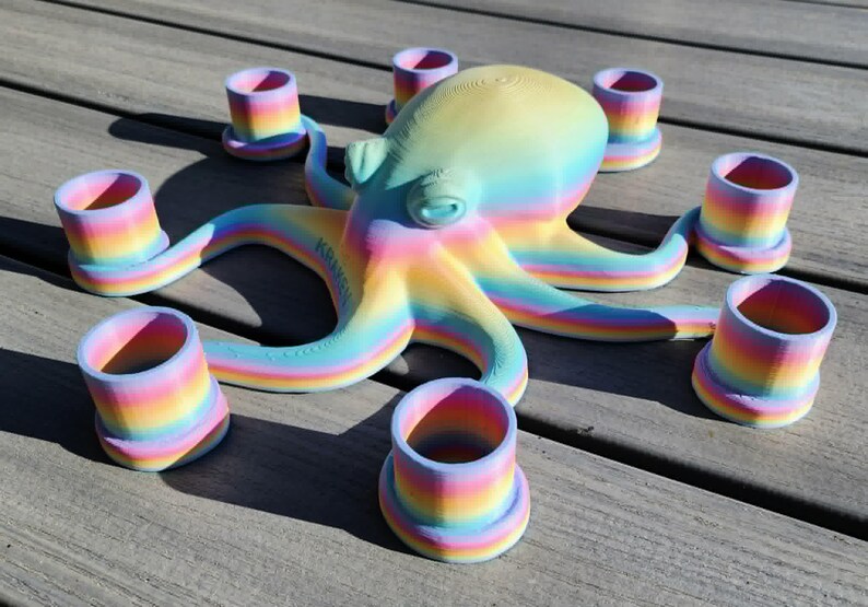 May include: A colorful octopus sculpture with eight matching cup-shaped candle holders. The octopus and candle holders are painted in a rainbow gradient of pastel colors. The sculpture is on a wooden surface.