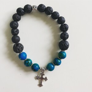 May include: A black lava rock and blue gemstone bracelet with a silver cross charm.
