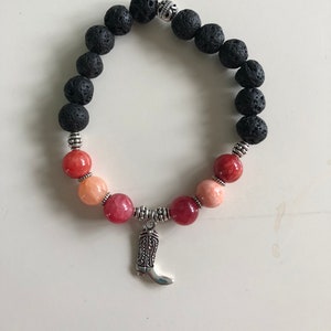 Può includere: Un braccialetto in pietra lavica nera con un ciondolo d'argento a forma di stivale da cowboy e perline di pietre preziose rosa e arancioni.