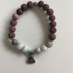 Puede incluir: Un brazalete de cuentas marrones y grises con un dije de plata. El brazalete está hecho de cuentas de lava y amatista.
