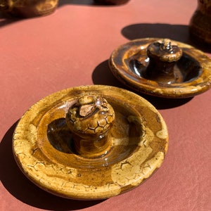 Op de afbeelding: Twee bruine keramische deksels met een verhoogde knop in het midden. De deksels hebben een getextureerd oppervlak met een honingraatpatroon.