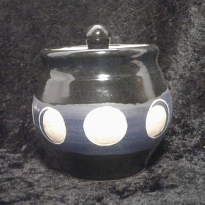 May include: A black ceramic jar with a lid, decorated with white moon phases on a blue band.