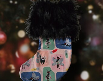 May include: A pink and green Christmas stocking with a black faux fur cuff. The stocking features a repeating pattern of colourful moths with glowing eyes.
