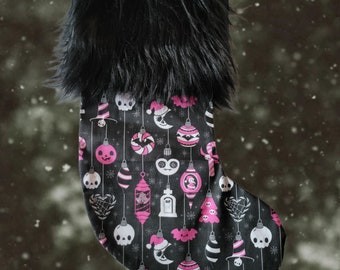 Puede incluir: Una media negra con un puño de piel sintética y un patrón rosa y negro de calaveras, murciélagos, bastones de caramelo y adornos. La media está colgada sobre un fondo nevado.