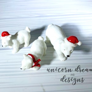 Può includere: Tre figurine di orso polare bianco che indossano cappelli rossi di Babbo Natale. Gli orsi polari sono in pose diverse. Il testo "unicorn dreams and designs" è visibile nell'angolo in basso a destra dell'immagine.