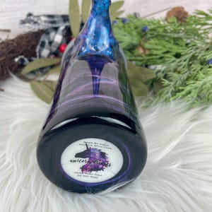 May include: A handcrafted, dark-colored bottle with a swirling blue and purple design. The bottle's base features a circular label with a unicorn illustration and the text "Unicorn Dreams Designs". The label also includes the text "Hand Wash Only, Do Not Soak".