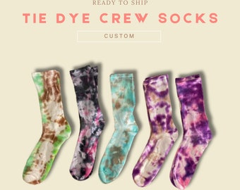 May include: Five pairs of tie-dye crew socks in different colour combinations. The socks are all white with different coloured tie-dye patterns. The colours include green, pink, blue, purple, and brown.