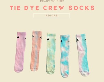 May include: Five pairs of tie-dye crew socks featuring the Adidas logo in black. The socks are in a variety of colours, including pink, orange, green, and blue.