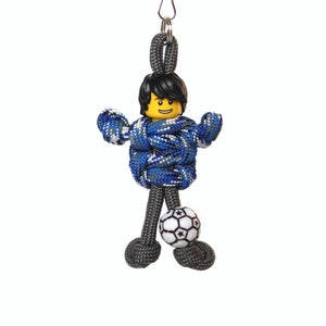 May include: A blue and gray paracord keychain with a Lego minifigure wearing a blue and white patterned shirt and holding a soccer ball.