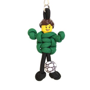 May include: Green paracord keychain with a Lego figure wearing a green shirt and holding a black and white soccer ball.