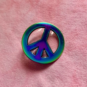 Puede incluir: Un pin con el símbolo de la paz en forma de arcoíris. El pin está hecho de metal y tiene un acabado brillante.
