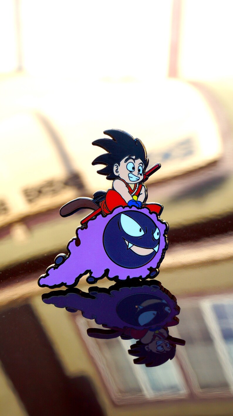May include: A colorful enamel pin featuring a cartoon character riding a purple ghost-like creature. The character is wearing a red and orange outfit with black hair. The ghost has a smiling face.