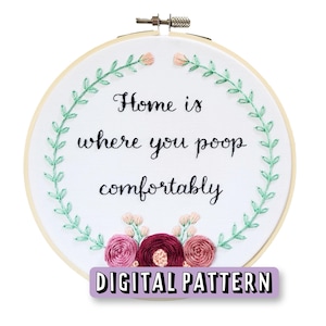 May include: Embroidered hoop art with a floral wreath and the text "Home is where you poop comfortably".