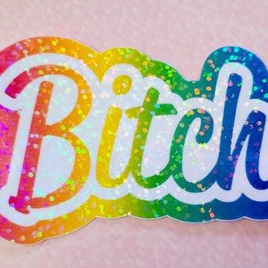 Könnte beinhalten: Ein regenbogenfarbener Aufkleber mit dem Wort "Bitch" in Weiß, umrandet von Schwarz. Der Aufkleber hat ein glitzerndes, irisierendes Finish und einen gewellten Rand. Der Hintergrund ist hellrosa.