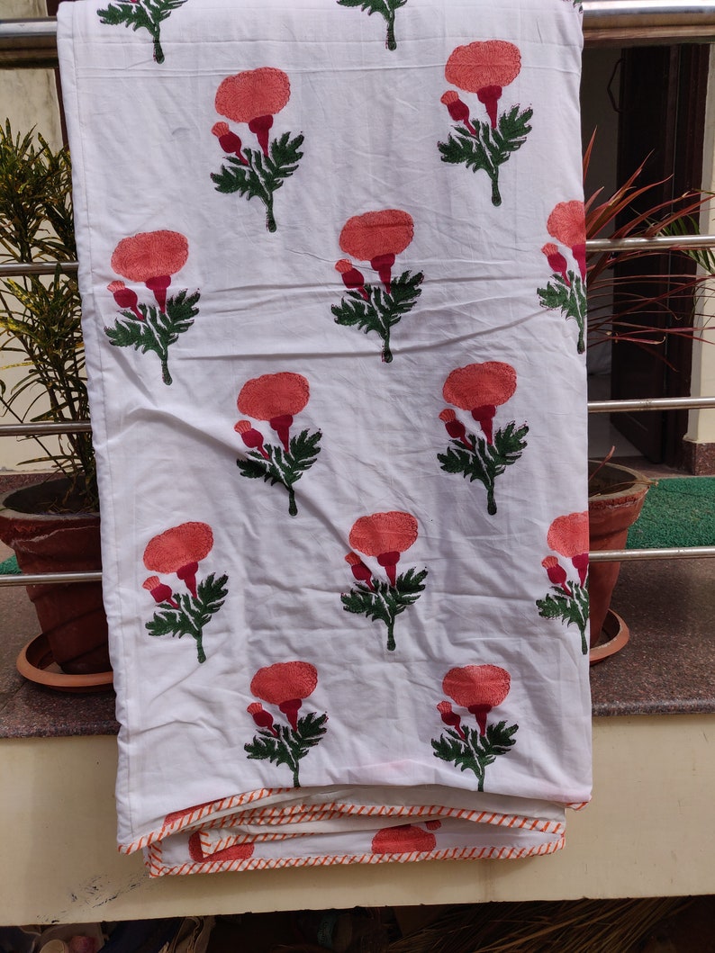May include: White cotton fabric with a repeating pattern of orange flowers with green leaves. The fabric has a white and orange trim around the edges.