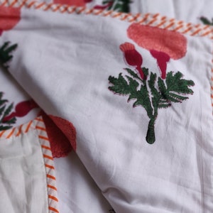 May include: White cotton quilt with a red and green floral print. The quilt has a white and orange striped border.