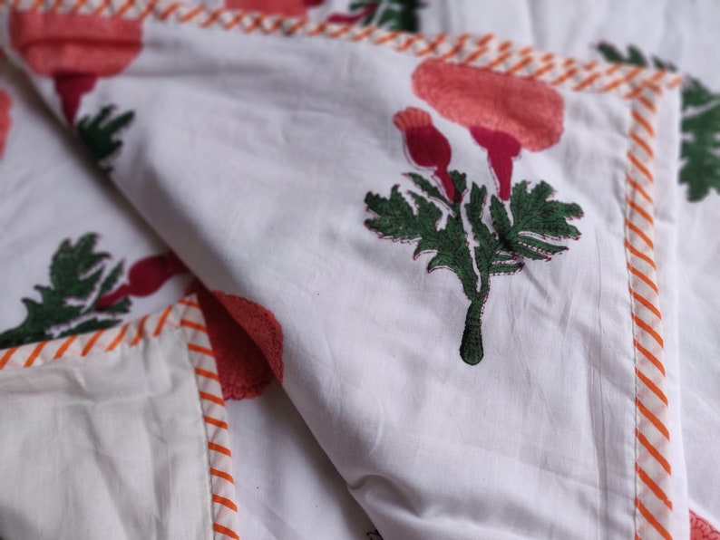 May include: White cotton quilt with a red and green floral print. The quilt has a white and orange striped border.